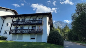 Ein zweistöckiges Gebäude mit Balkonen, eine Straße im Vordergrund und Berge im Hintergrund.