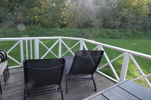 An outdoor deck with a white railing, two black chairs, and a wooden table.