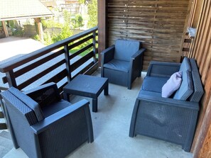 Ein Patio mit Korbmöbeln, darunter eine Couch und Stühle, sowie ein Holzzaun im Hintergrund.
