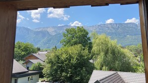 A mountain landscape through a window with a wooden frame, houses, and trees in the foreground. - Apartment near the lake with a terrace offering mountain views. (Doussard)