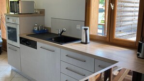 A modern kitchen with a central island, built-in oven, and a large window with a view of the outdoors. - Apartment near the lake with a terrace offering mountain views. (Doussard)
