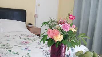 Una cama con colcha estampada, un jarrón con flores y un frutero sobre una mesita de noche.