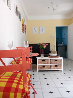 Une pièce comprenant une table à manger, des chaises, un meuble blanc avec des paniers et une porte bleue donnant sur une salle de bain.