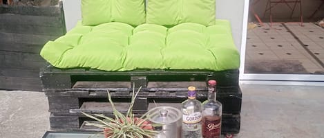A green cushioned bench with a metal frame, a black coffee table with a patterned rug, and a potted plant.