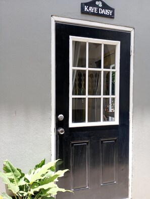 A black door with a white-framed window and a sign above it that reads 'KAYE DAISY'.