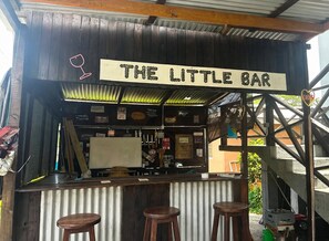 Un bar rústico llamado 'The Little Bar' con una barra de madera, taburetes y diversos carteles y adornos.