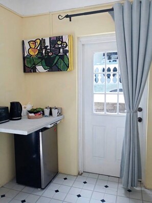 A compact kitchen area with a refrigerator, a coffee maker, and a small table with cups and a basket. - 1-bedroom apartment 5 minutes from airport/Bar and grill onsite (Eau Piquant)