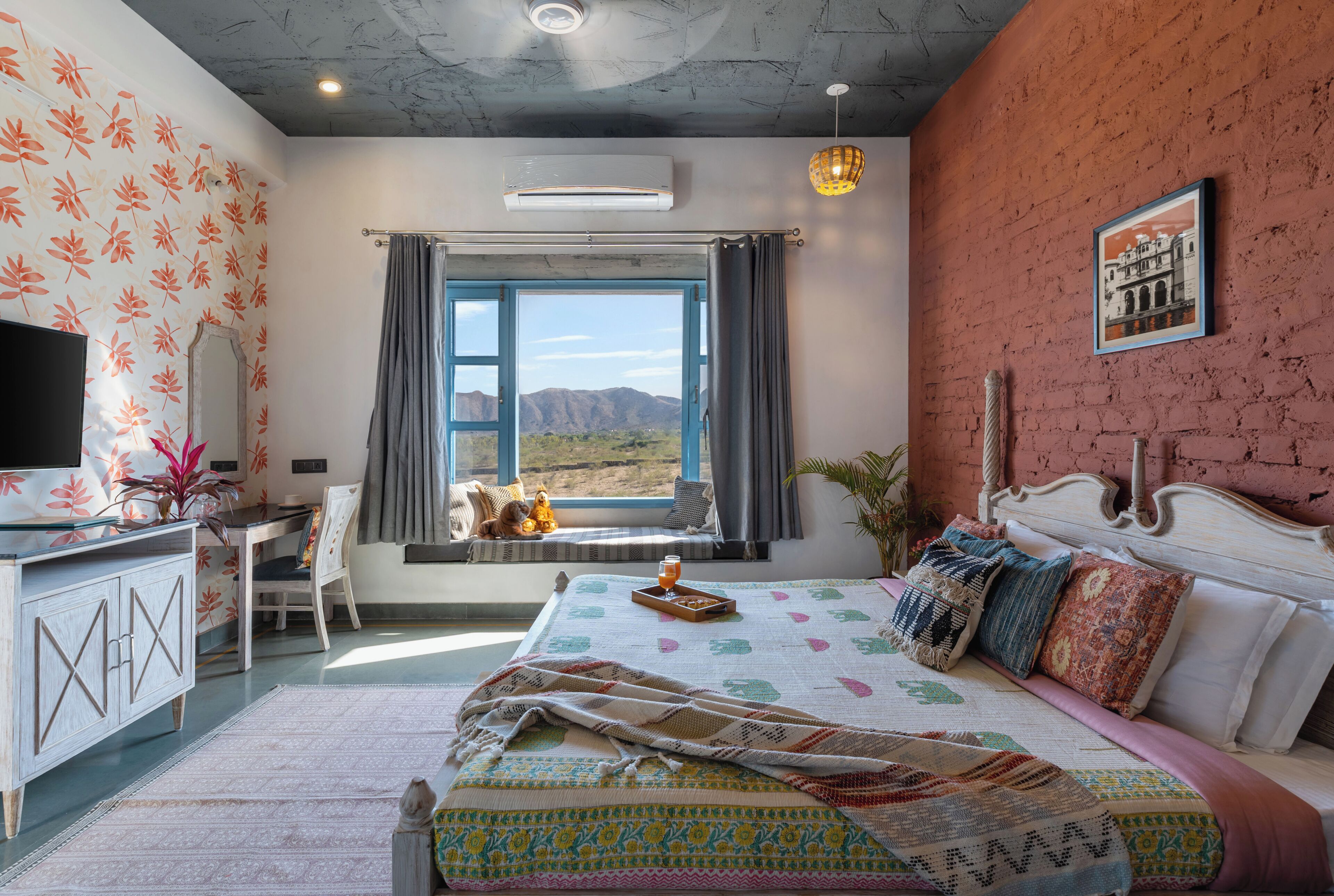 A bedroom with a bed, a desk, a chair, a window with a view of mountains, and a television.
