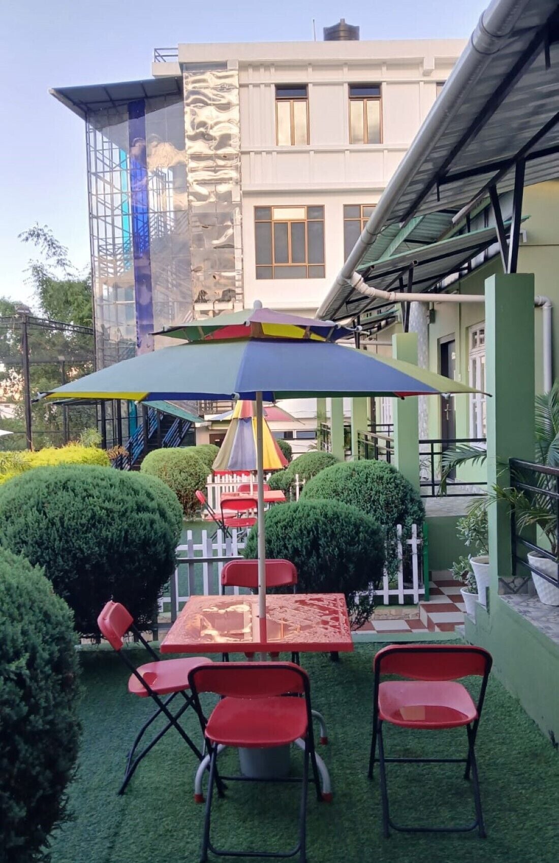 An outdoor seating area with tables and chairs, a colorful umbrella, and a building in the background.