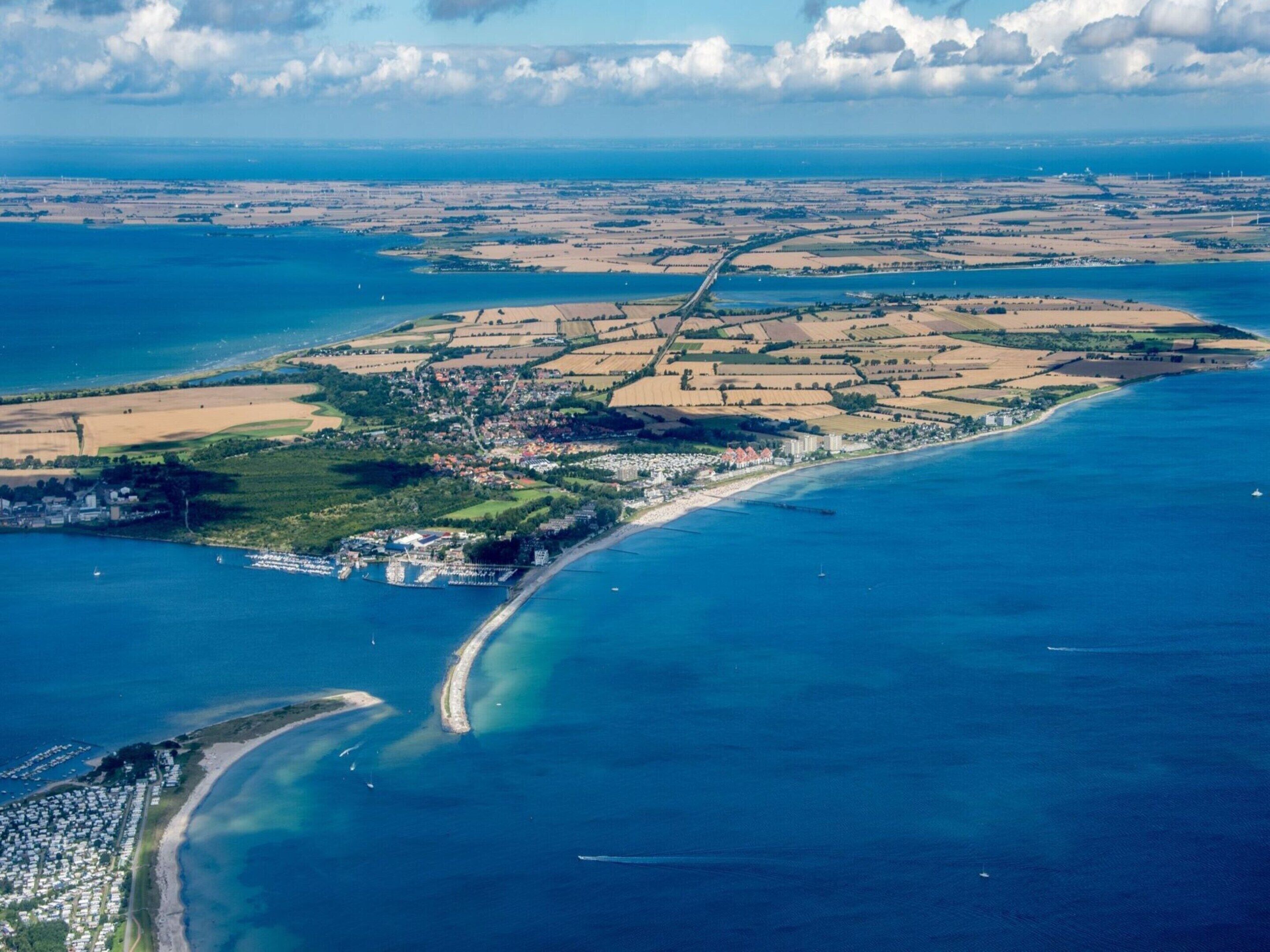 An aerial view of a coastal area with a mix of residential and agricultural land, a curved coastline, and a small settlement with buildings near the shore.