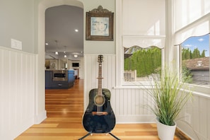 A room with a guitar, a potted plant, and a view of the outdoors.