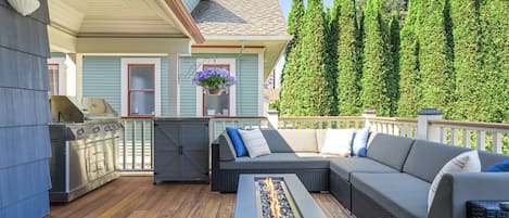 A covered outdoor deck with a grill, seating area, and a fire feature.