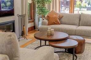 A living room with a sofa, two round coffee tables, a fireplace, and a large window with a view.