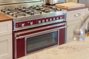 Une cuisine équipée d’une cuisinière à gaz, d’un four et d’une planche à découper en bois posée sur le plan de travail.