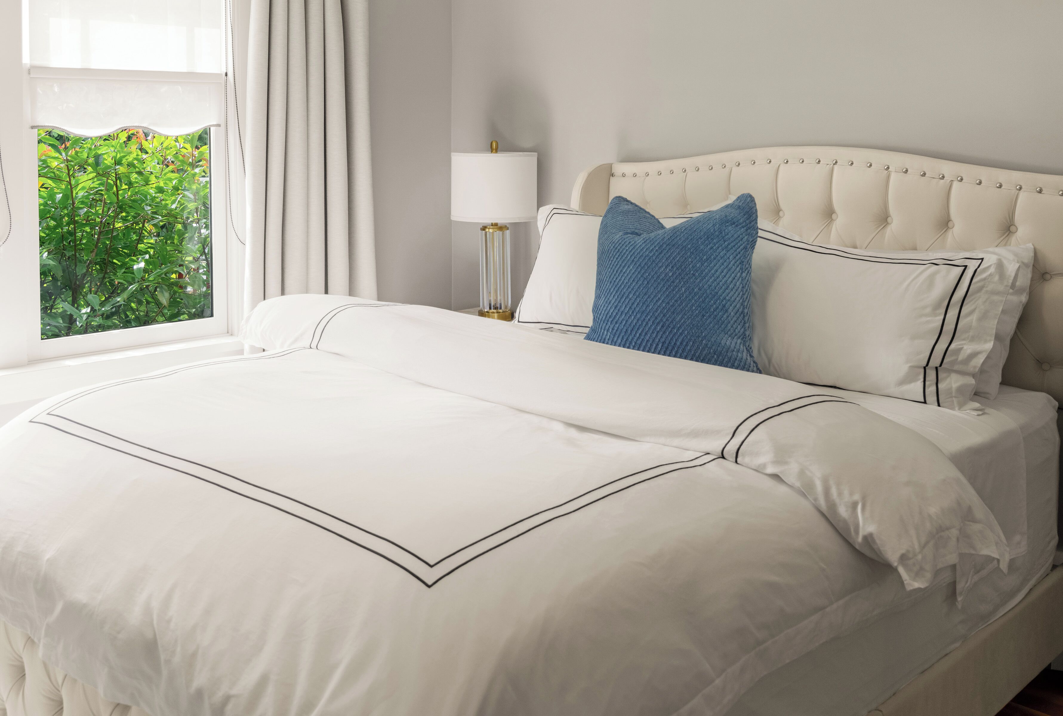 A neatly made bed with a white duvet, a blue pillow, and a white pillow with a black trim.