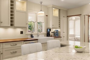 A kitchen with white cabinetry, a marble countertop, and a coffee maker. - Lovingly restored 1932 heritage home offering vintage feel with modern comfort. (New Westminster)