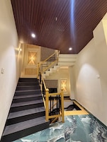 A staircase with a wooden handrail and black steps, leading to a landing with a light fixture.