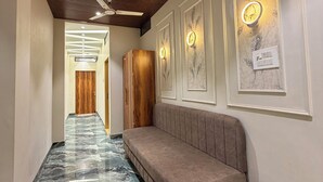 Un pasillo con suelo de mármol, un banco de madera y lámparas fijadas a la pared.