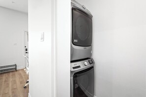 A compact, modern laundry room with a stacked washer and dryer, a bench, and a door leading to another room.