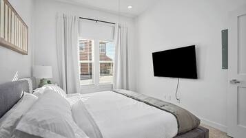 Ein Schlafzimmer mit Bett, einem an der Wand montierten Fernseher, einem Fenster mit Vorhängen und einer Tür.