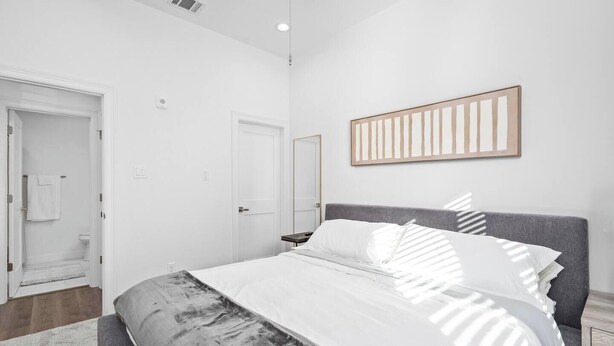 Ein modernes Schlafzimmer mit einem großen Bett, einem Nachttisch, einem Kleiderschrank und einem durchgegangenen Tür sichtbaren Badezimmer.