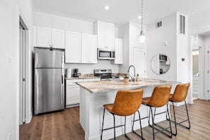 A modern kitchen with white cabinets, stainless steel appliances, a marble island with bar stools, and a pendant light.