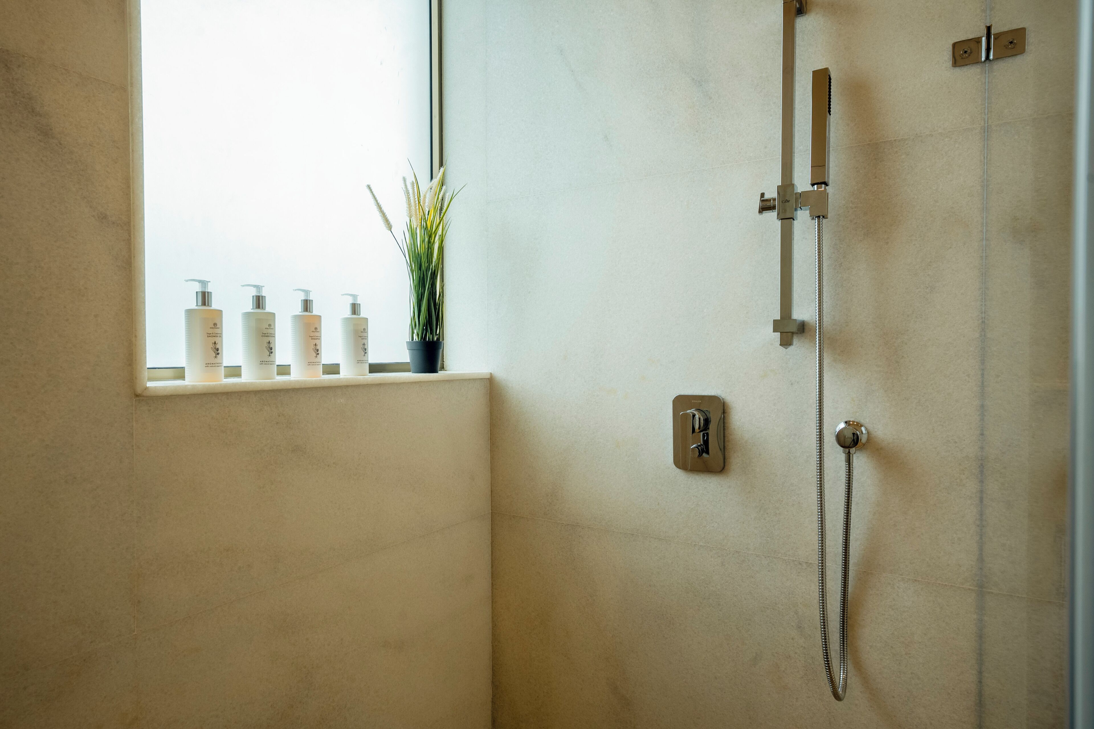 A bathroom with a shower, a window with bottles, and a plant.