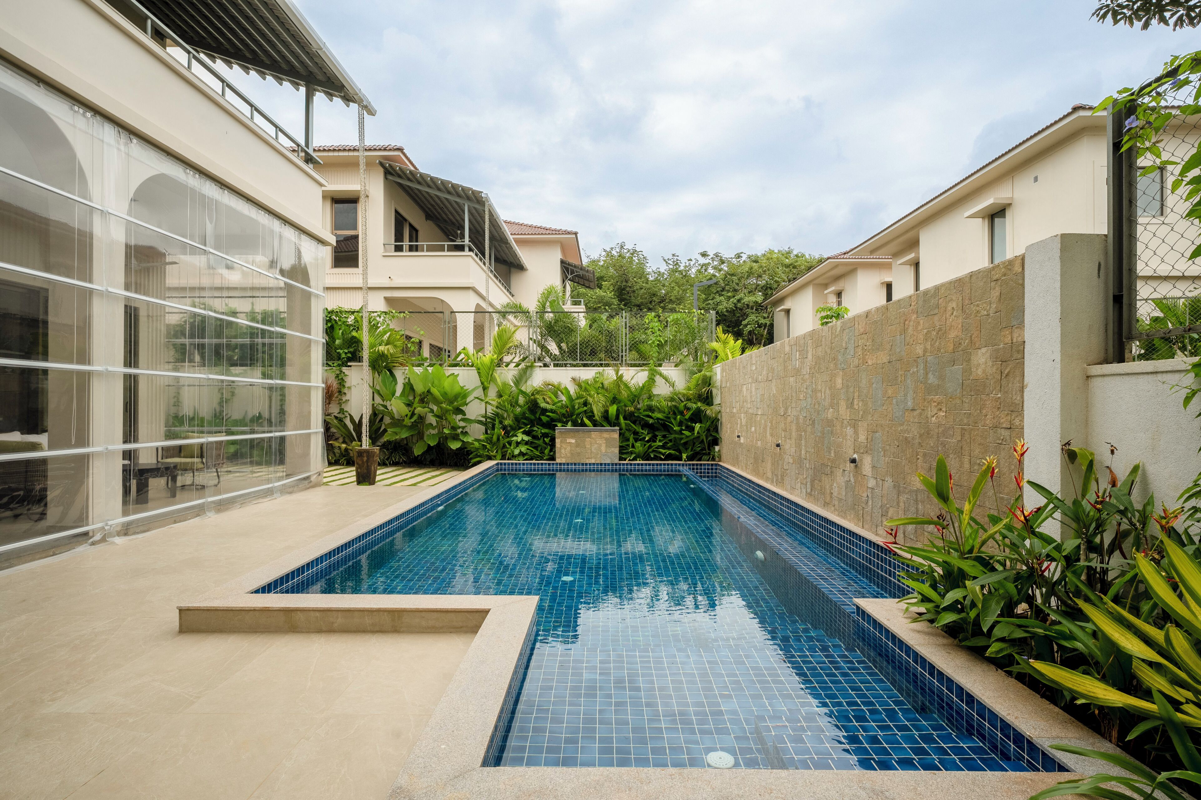 A swimming pool with a tiled edge, surrounded by a low stone wall and lush greenery.