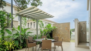 Een terras buiten met een ronde tafel en stoelen, omringd door verschillende planten.