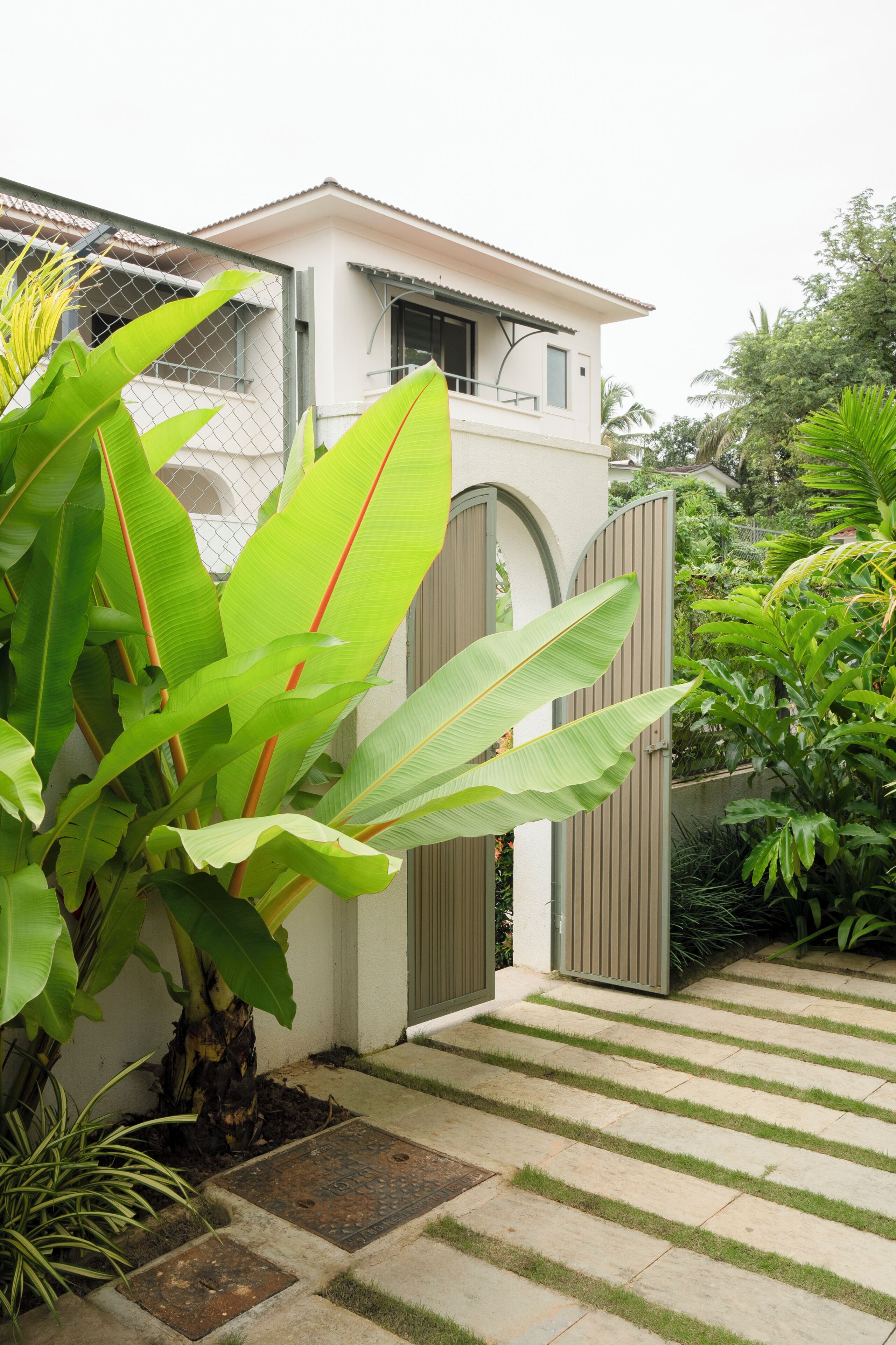 Edificio residencial con entrada porticada, camino de acceso pavimentado y exuberante vegetación tropical.