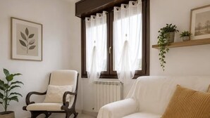 Un saló amb un sofà blanc, una cadira bressol, una alfàbrega rodona i un radiador.