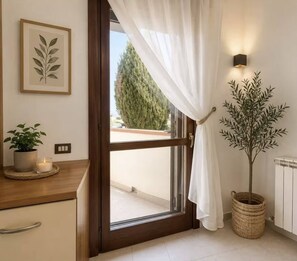 Ein Zimmer mit Holztür, Blumentopf, gerahmtem Pflanzenmotiv und einer Wandleuchte.