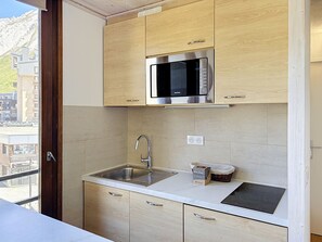A compact kitchen with a stainless steel sink, a microwave, and wooden cabinets. - Les Grandes Platières (Val Claret) by Interhome (Tignes)