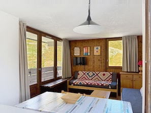 A room with a wooden bench, a table, a television, and a window with curtains. - Les Grandes Platières (Val Claret) by Interhome (Tignes)