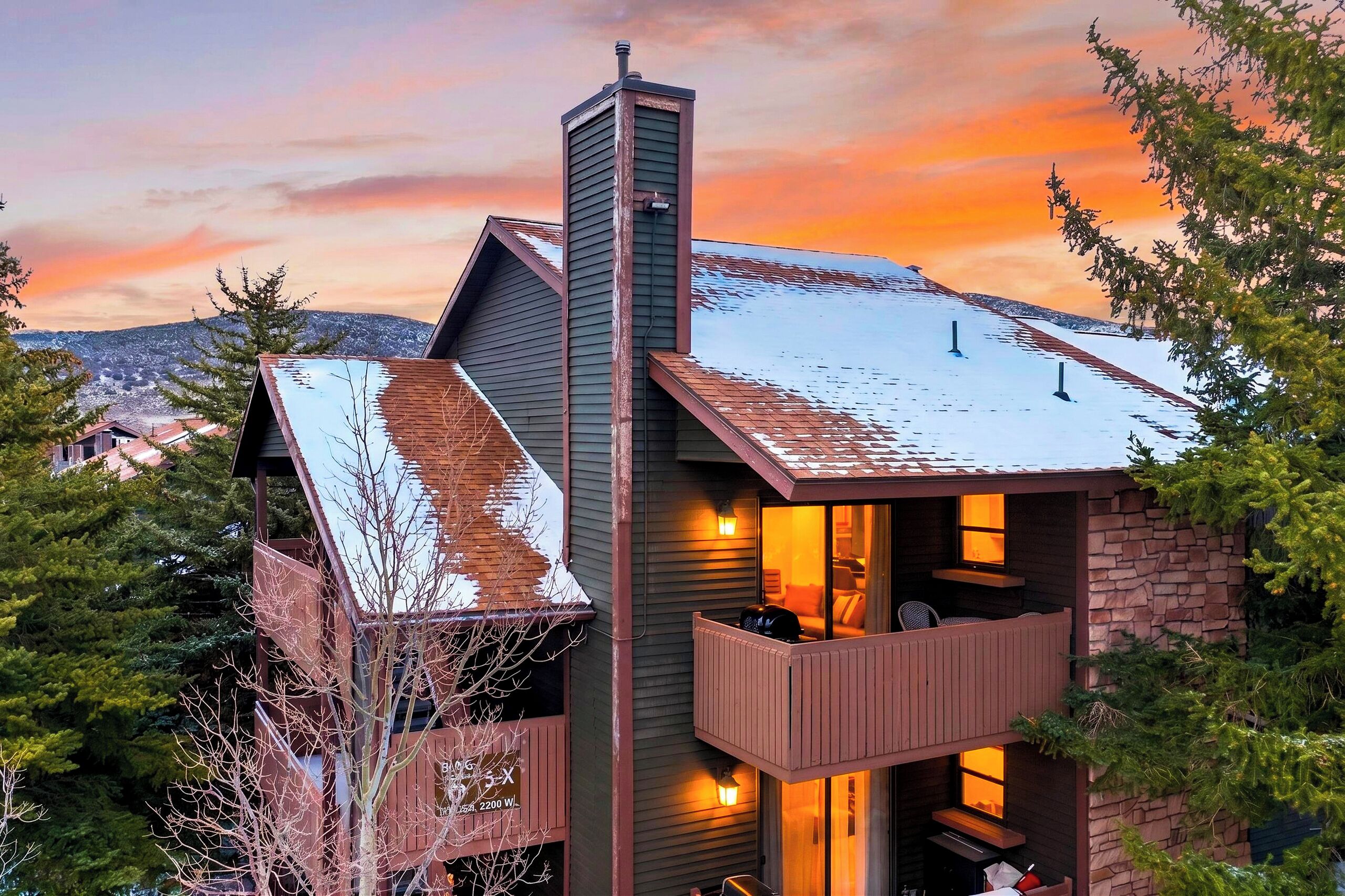 A two-story house with a balcony and a chimney, surrounded by trees and a snowy landscape.