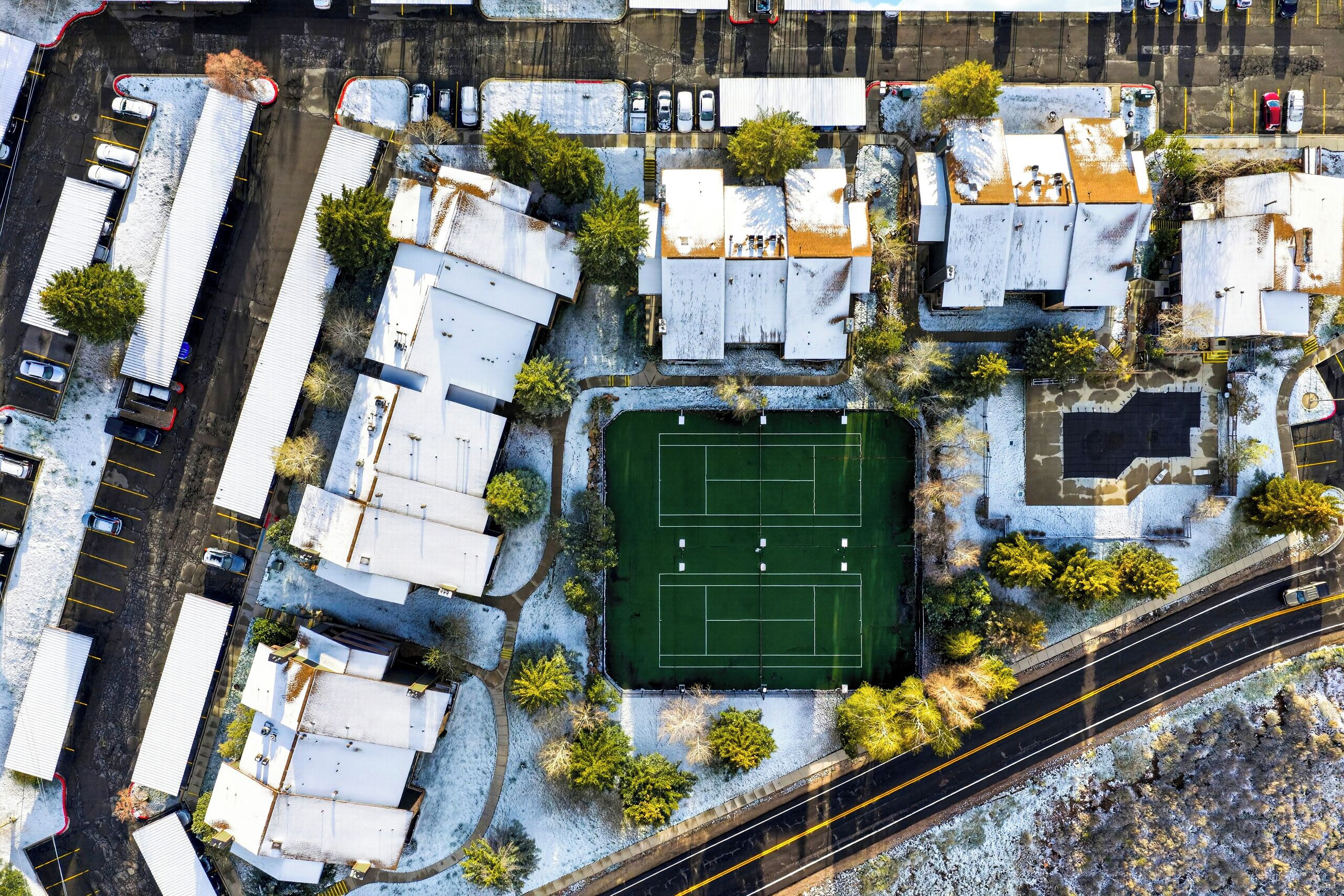 An aerial view of a parking lot with multiple buildings, a green sports field, and a road with a curve.