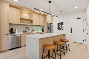 A modern kitchen with wooden cabinets, stainless steel appliances, a white countertop, and three bar stools.