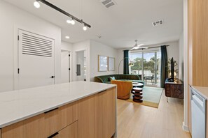 A modern kitchen with a white countertop and wooden cabinets, a green sofa, and a dining area with a table and chairs.