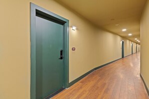 A hallway with doors, a wooden floor, and a light fixture on the wall.