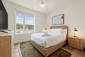 A bedroom with a bed, a nightstand, a desk, a window with a view, and a ceiling fan. - 4BDR South Lamar Stay w/ Pool, Rooftop, Restaurant | The Code by AvantStay (Austin)