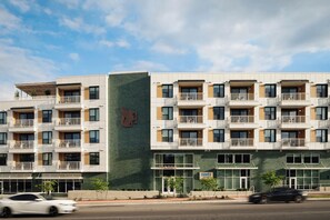 A multi-story hotel with balconies, a prominent logo on the facade, and a sign indicating a restaurant. - 4BDR South Lamar Stay w/ Pool, Rooftop, Restaurant | The Code by AvantStay (Austin)