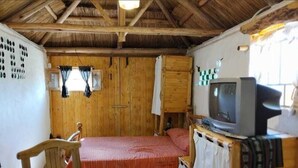 A room with a bed, a television on a wooden stand, a table with a bowl, and a window with curtains.