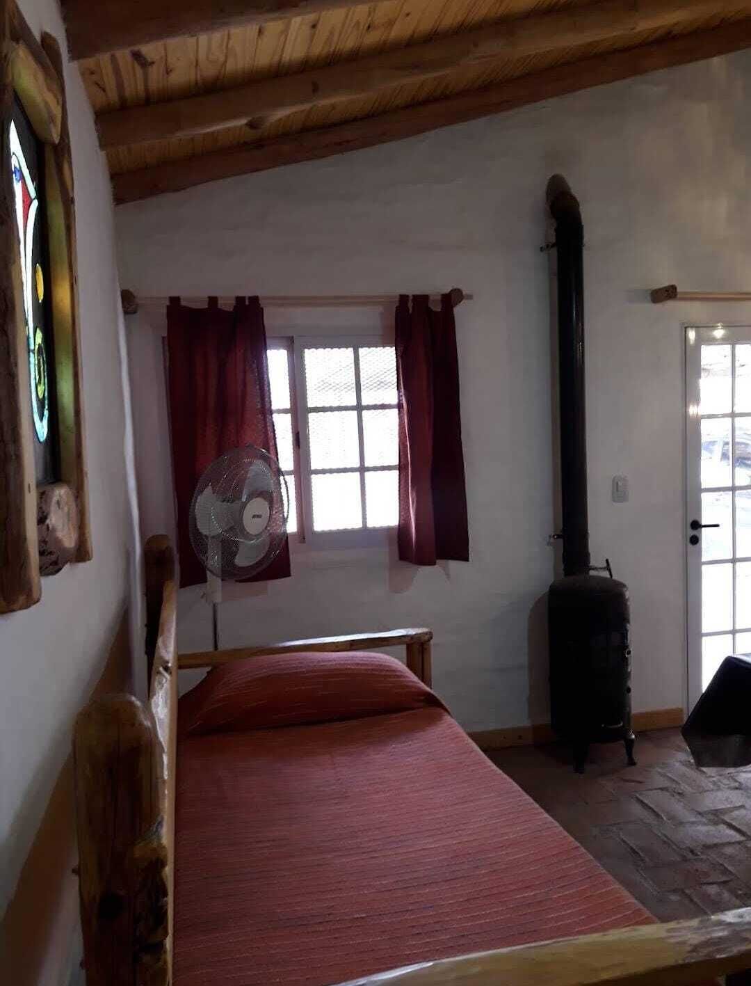 Ein Zimmer mit einem Bett, einem Ventilator, einem Fenster mit Vorhängen und einem Herd.