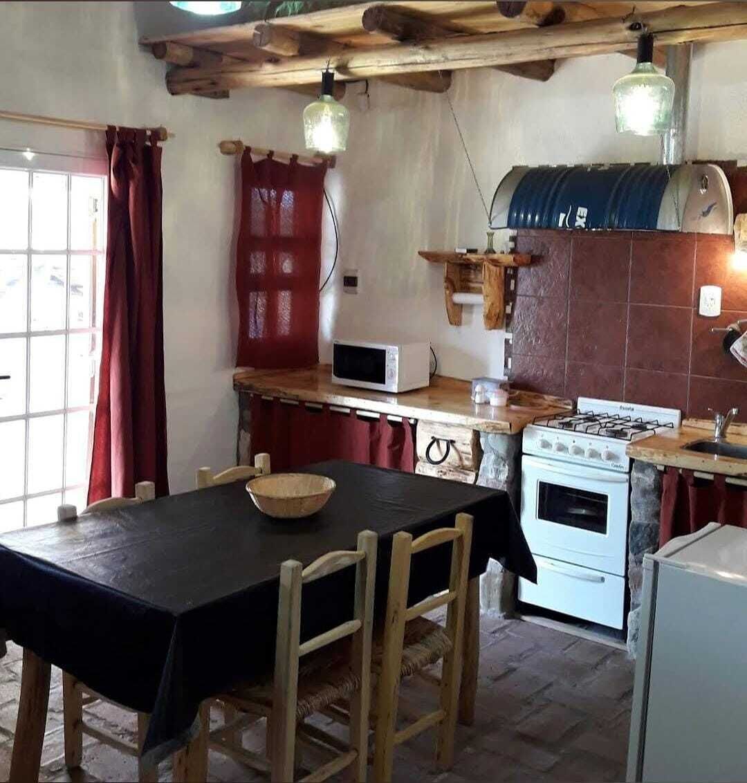 A rustic kitchen with a wooden table, chairs, a stove, a microwave, and hanging light fixtures.