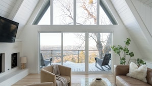 A spacious loft with a high ceiling, large windows, and a view of a snowy landscape. - A-Frame Cabin w/ Hot Tub + Firepit | EV Charger + Steps to Trails | The A-List (Lake Arrowhead)