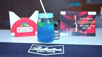 Una caja de cerveza Kingfisher Strong, una bebida azul en un vaso y un folleto promocional de Louis Baron sobre una mesa.