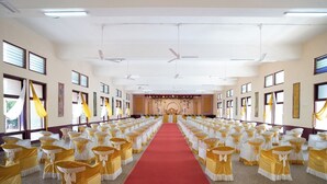 A large hall with rows of chairs, a red carpet, and ceiling fans.