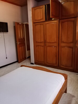A bedroom with a bed, wooden wardrobe, and a television mounted on the wall. - Superb 6-bedroom apartment with AC in Takoradi, best location and beautiful area (Takoradi)