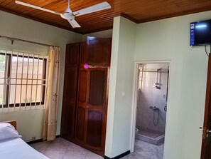 A room with a bed, a wooden wardrobe, a shower, and a ceiling fan. - Superb 6-bedroom apartment with AC in Takoradi, best location and beautiful area (Takoradi)