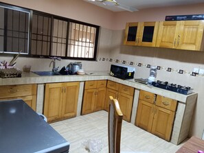 A kitchen with wooden cabinets, a microwave, a gas stove, and a window with bars. - Superb 6-bedroom apartment with AC in Takoradi, best location and beautiful area (Takoradi)